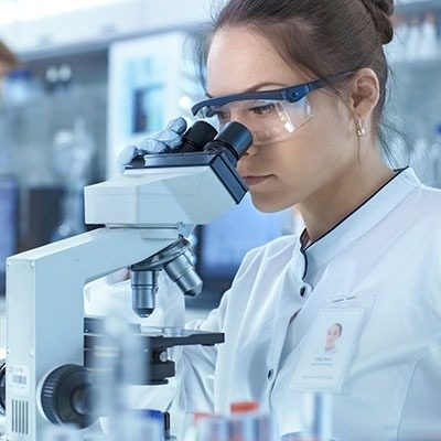 Medical Research Scientists Looking at Samples Under Microscope. She Works in a Bright Modern Laboratory.